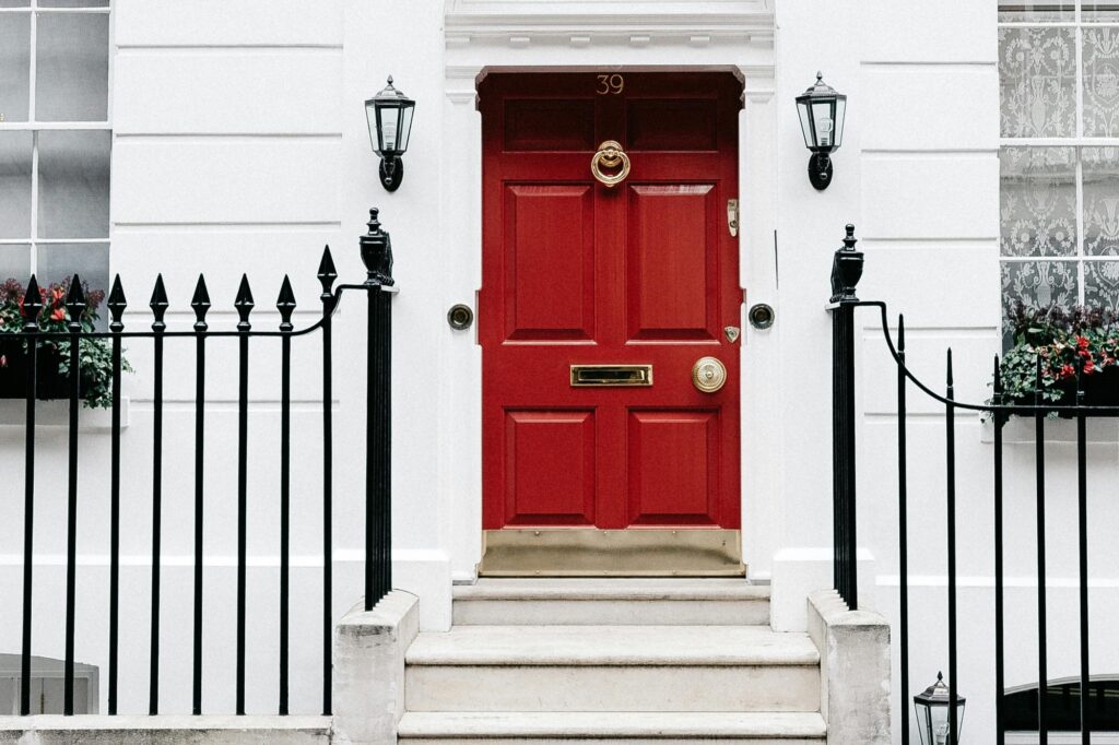 In front of a white-coloured townhouse with railings and red door, in the concept of housing options in Slough